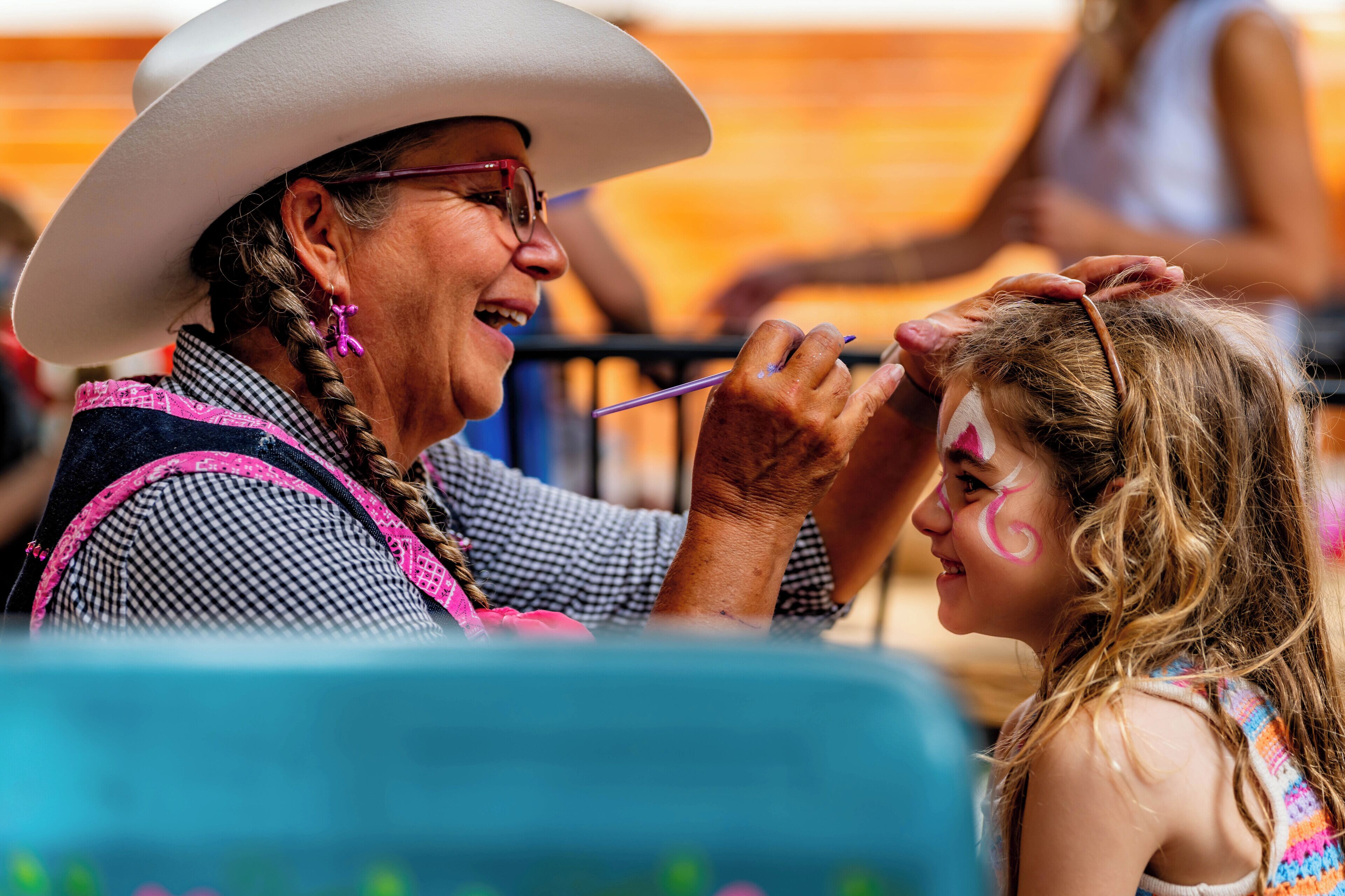 A person in a cowboy hat and checkered shirt painting another person's face.