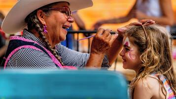 A person in a cowboy hat and checkered shirt painting another person's face.