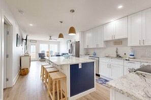 Una cocina moderna con armarios blancos, una isla central, taburetes de madera e iluminación colgante.