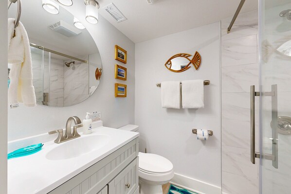 Un baño moderno con un tocador blanco, cabina de ducha de vidrio y pared de mármol.