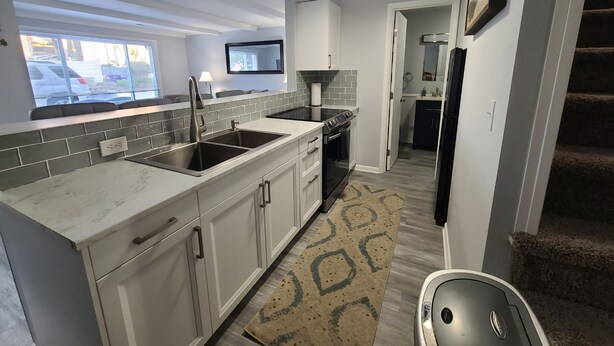 A modern kitchen with white cabinets, a black stove, and a large window overlooking a parking lot. - Cozy boathouse located at the Cedar Point entrance!  (Sandusky)