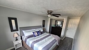 A bedroom with a bed, nightstand, dresser, ceiling fan, and a door leading to another room. - Cozy boathouse located at the Cedar Point entrance!  (Sandusky)