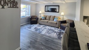 A spacious living area with a large window, a sofa set, a coffee table, and a flat-screen TV mounted on the wall. - Cozy boathouse located at the Cedar Point entrance!  (Sandusky)