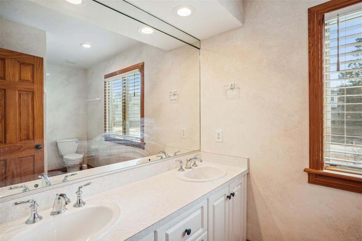 A bathroom with a double sink, a large mirror, and a window with blinds.