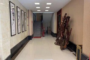 A hallway with framed artwork on the walls, a staircase in the background, and a wooden sculpture on the floor. - Sanming Zunhe Inn (Shaxian Snack Culture City) (Sanming)