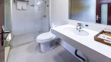 A bathroom with a glass-enclosed shower, a white toilet, and a sink with a mirror above it.