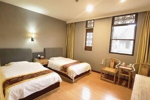 A hotel room with two beds, a small table, two chairs, a nightstand, and a window with curtains.