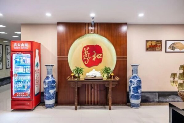 A reception area with a red vending machine, two blue vases, and a wooden table with a decorative item.