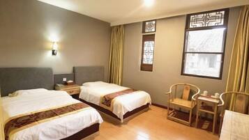 A hotel room with two beds, a small table, two chairs, a nightstand, and a window with curtains.