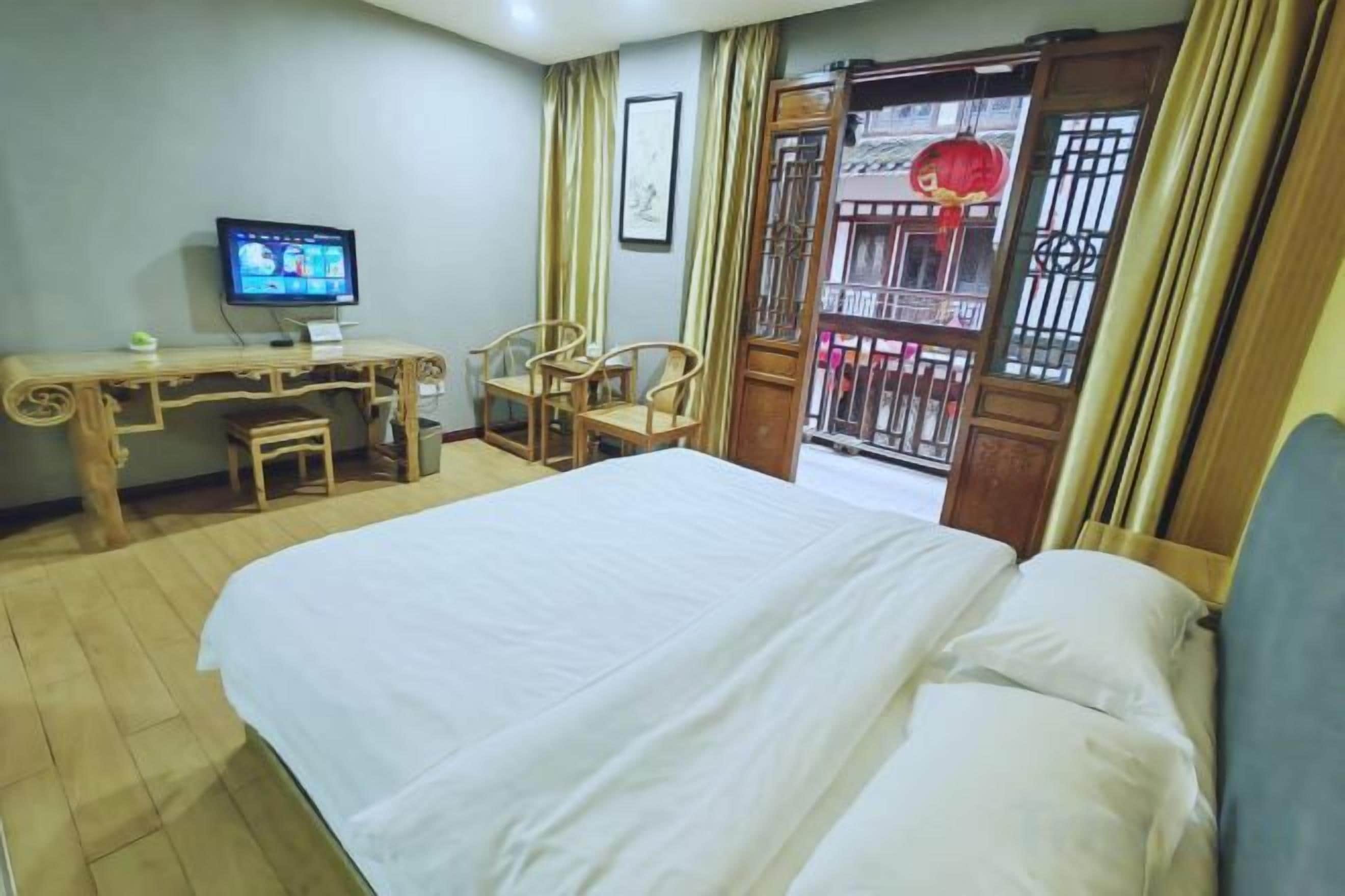 A hotel room with a bed, desk, chairs, a television, and a balcony with a view.
