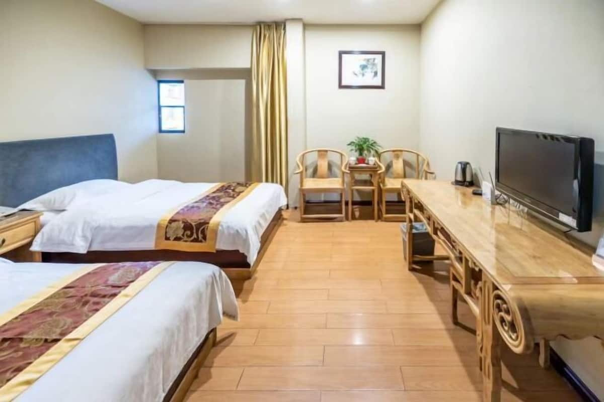 Ein Hotelzimmer mit zwei Betten, einem Holztisch, Stühlen, einem Fernseher und einem kleinen Tisch mit Pflanze und Wasserkocher.