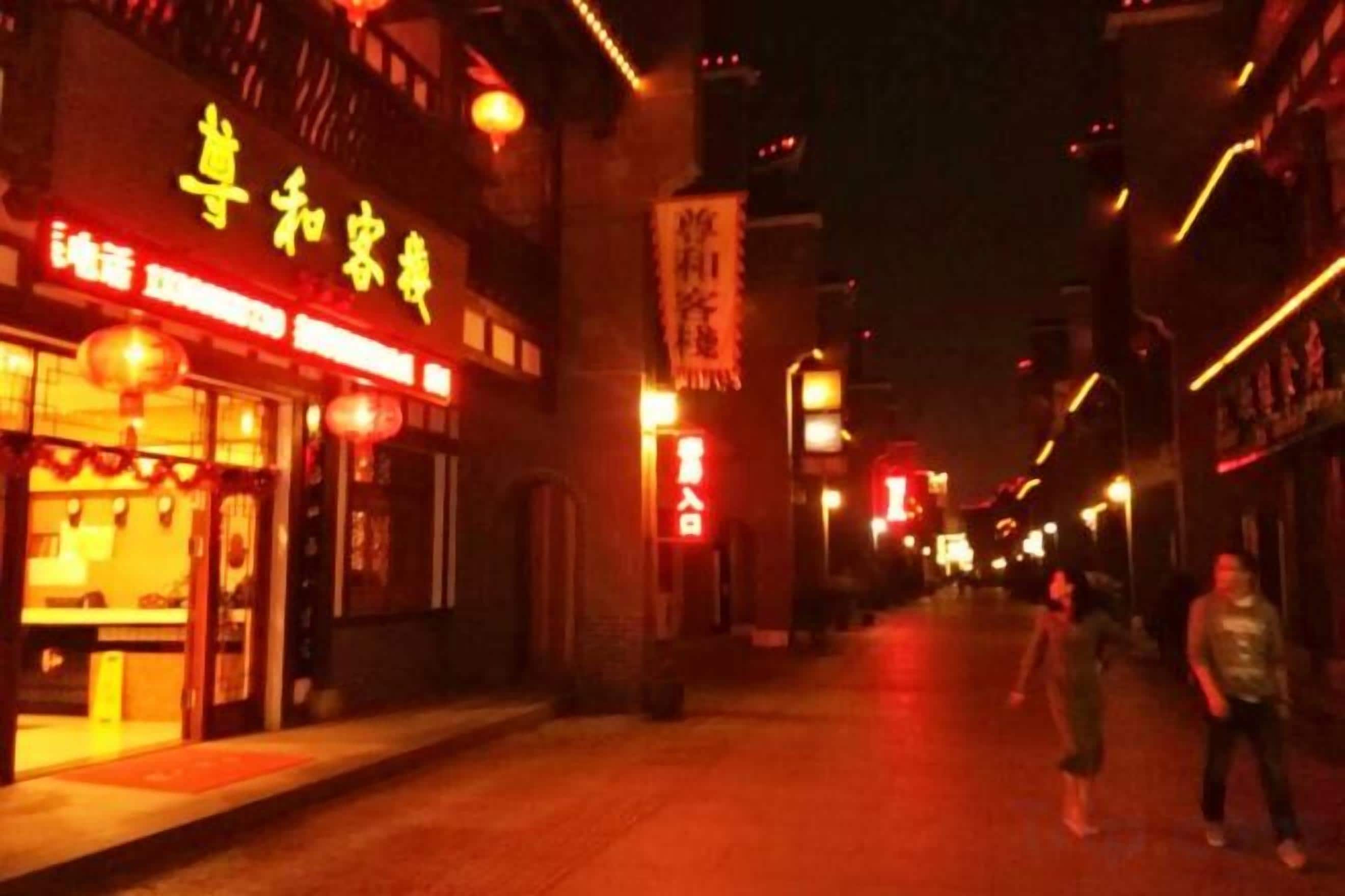 A street at night with illuminated storefronts and a pedestrian walkway.
