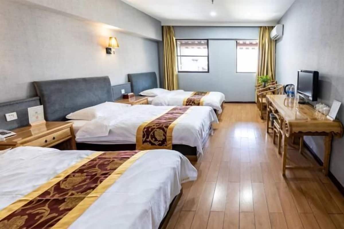 Ein Hotelzimmer mit drei Betten, einem Schreibtisch, einem Fernseher und einem Fenster mit Vorhängen.