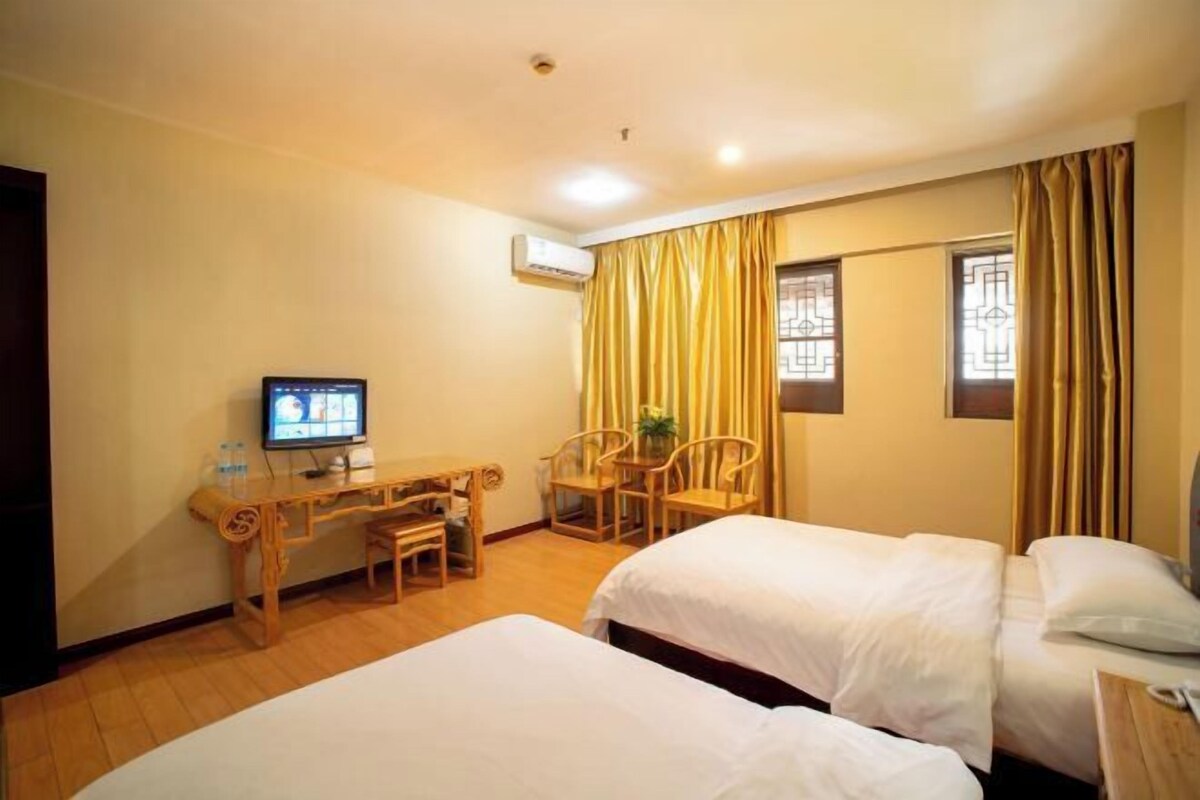 A hotel room with two beds, a desk with a chair, a television, and curtains.