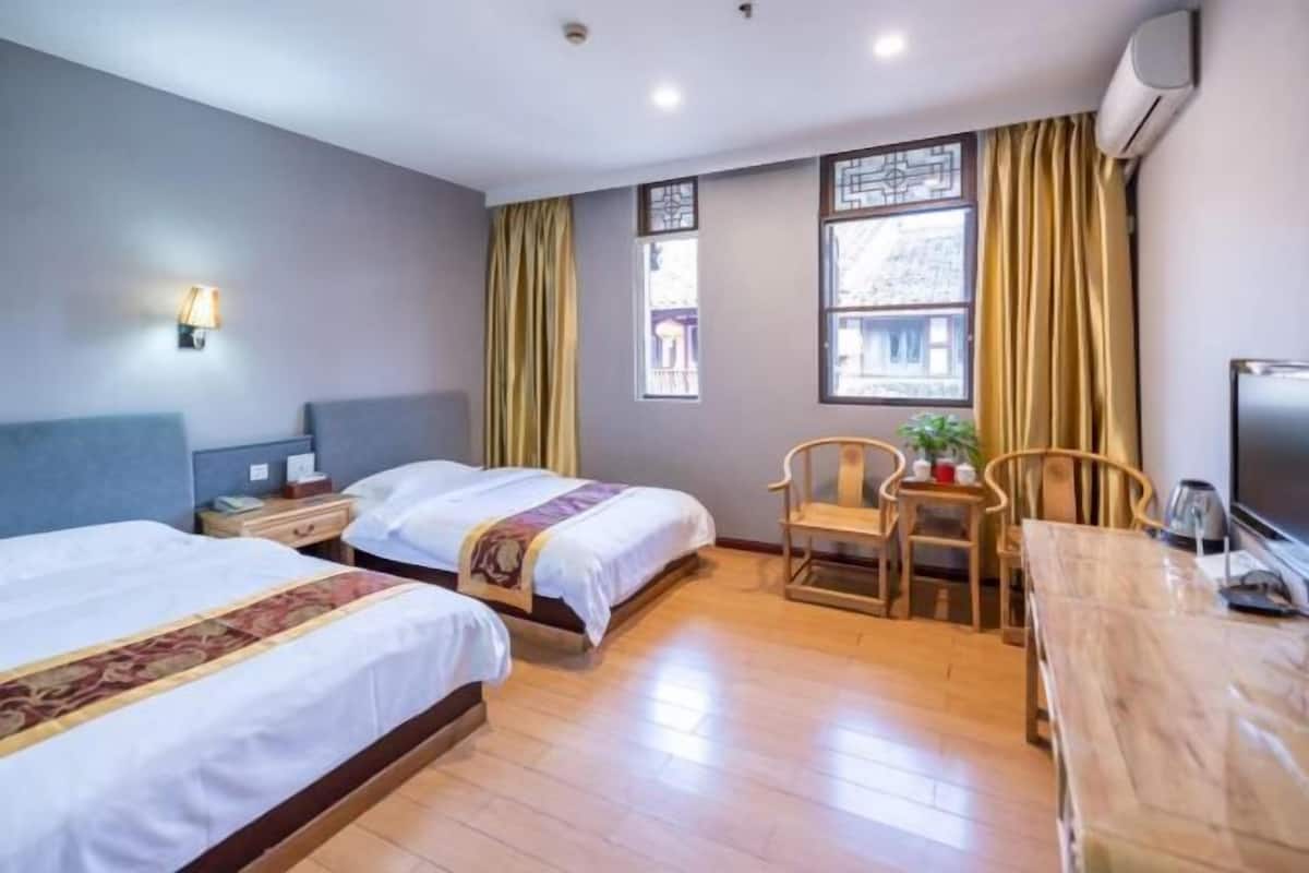 Ein Hotelzimmer mit zwei Betten, einem Holztisch, einem Stuhl, einem Fernseher und einem Fenster mit Vorhängen.