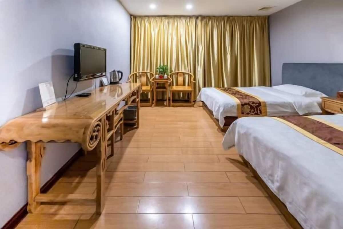 Ein Hotelzimmer mit einem Holztisch, zwei Betten, einem Fernseher und einem Vorhang.