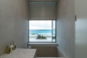 A bathroom with a large window overlooking a beach, a sink, and three bottles of liquid.