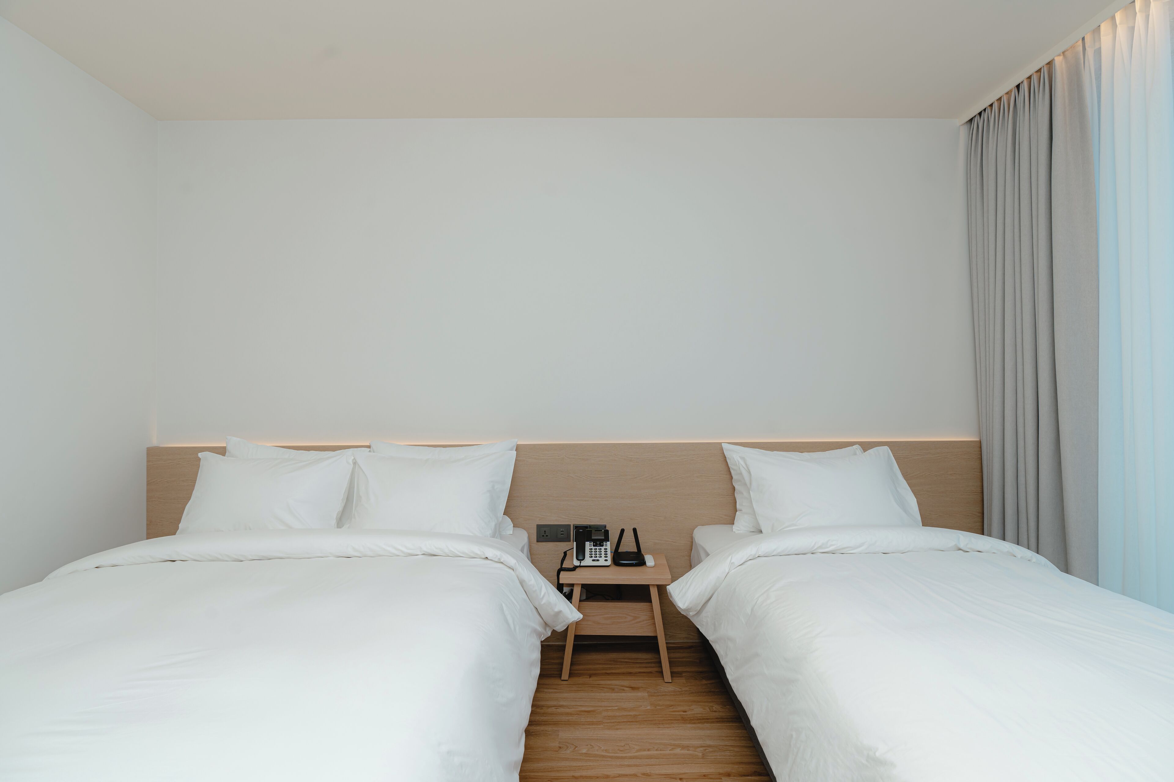 A hotel room with two single beds, a wooden nightstand, and a telephone.