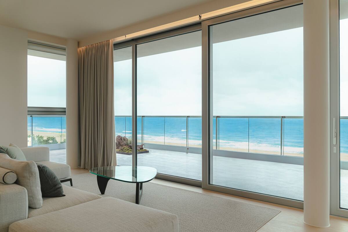 Una sala de estar moderna con una mesa de vidrio, un sofá y vistas a la playa a través de grandes puertas correderas de cristal.