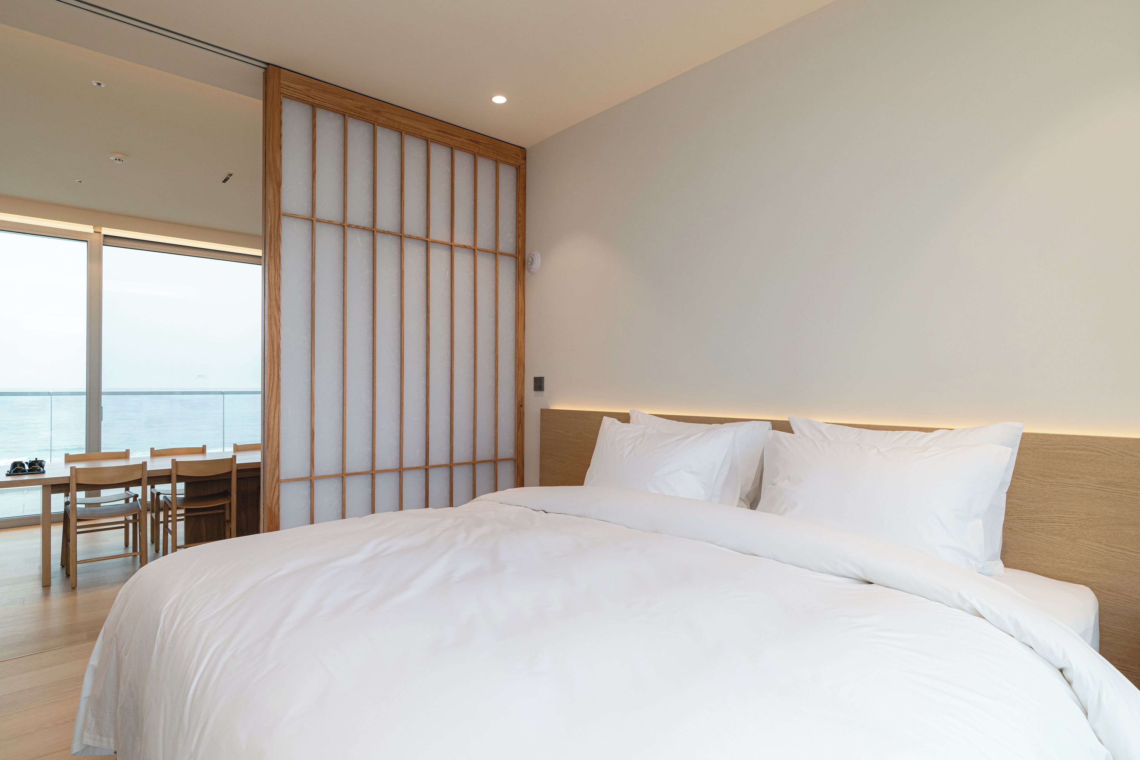 A modern hotel room with a large bed, a wooden desk, and a view of the sea.