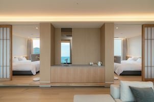 A modern hotel room with a central island, two beds, a sofa, and a view of the sea.