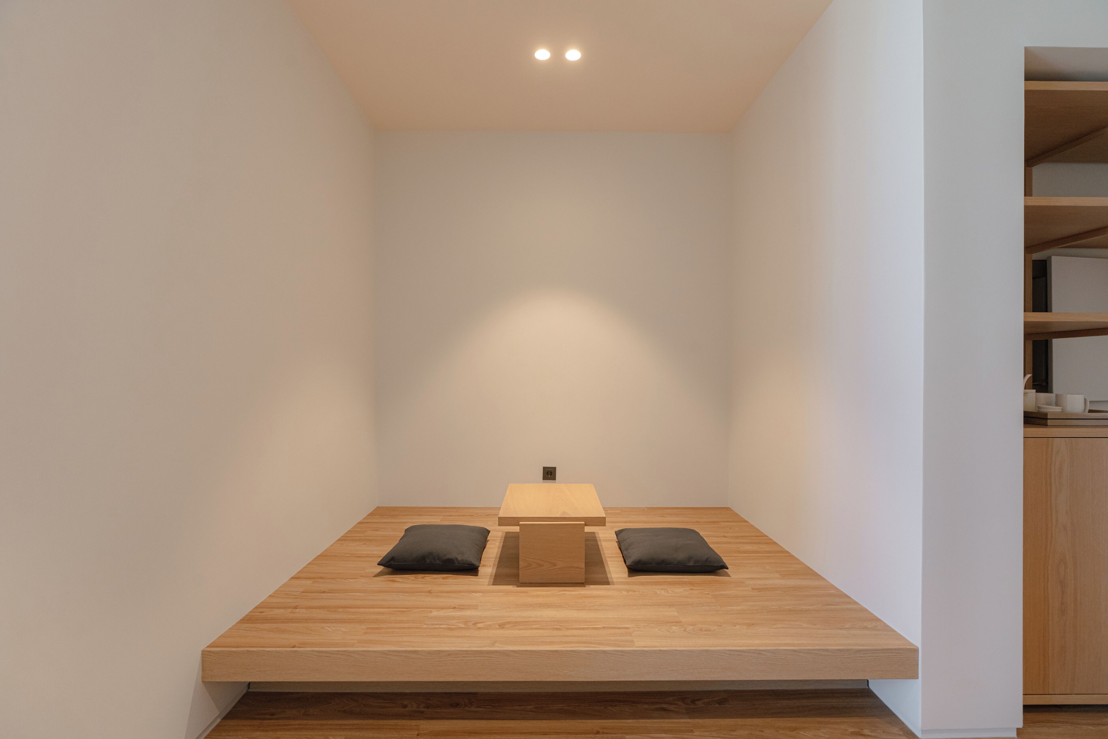 A minimalist room with a wooden platform table, two black cushions, and a small wooden box.