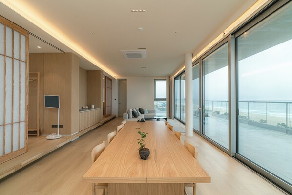 Una sala de conferencias moderna con una larga mesa de madera, una planta en maceta y grandes ventanales con vistas al océano.