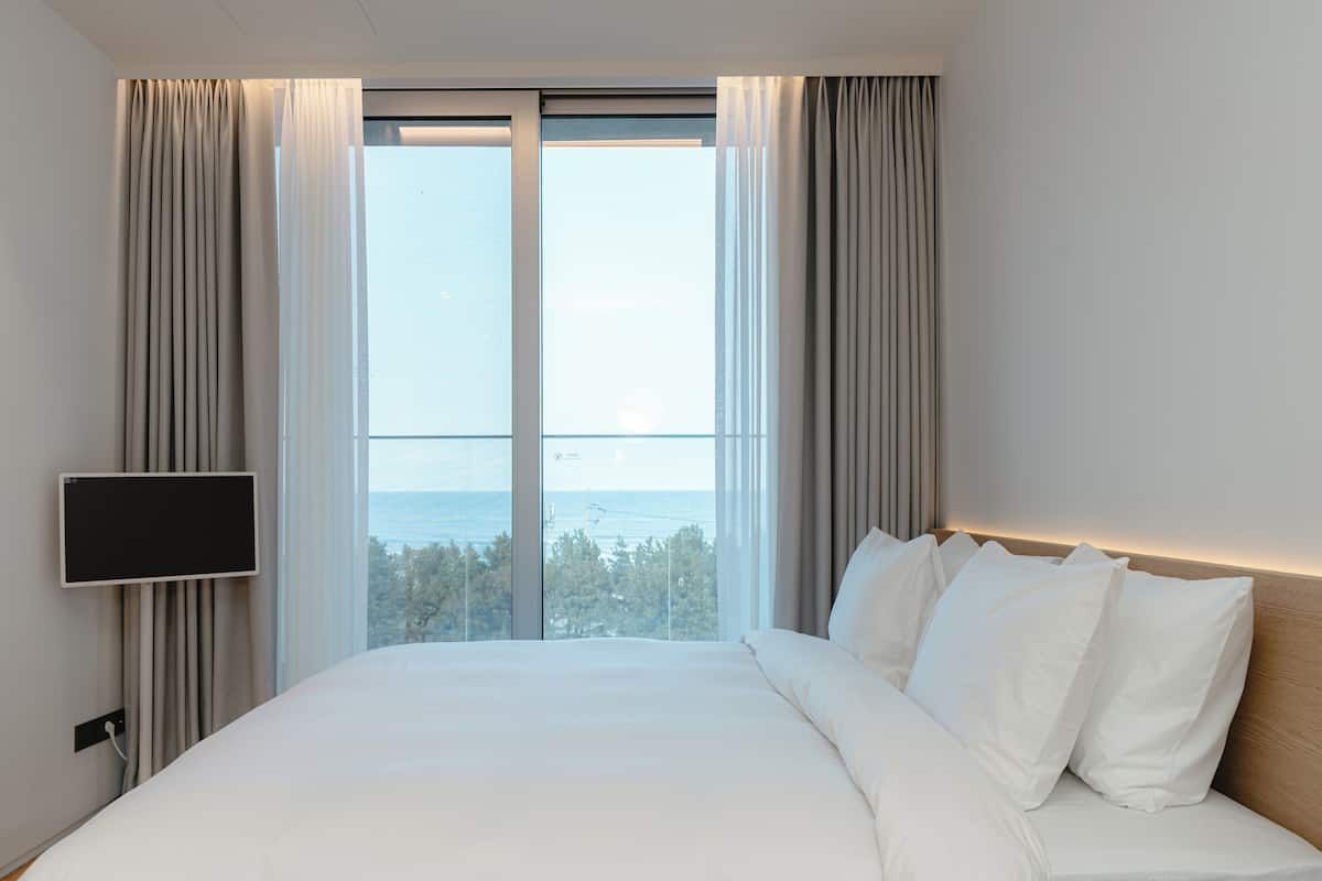 Habitación de hotel con una cama grande, un televisor de pantalla plana y vista al mar a través de un ventanal amplio.