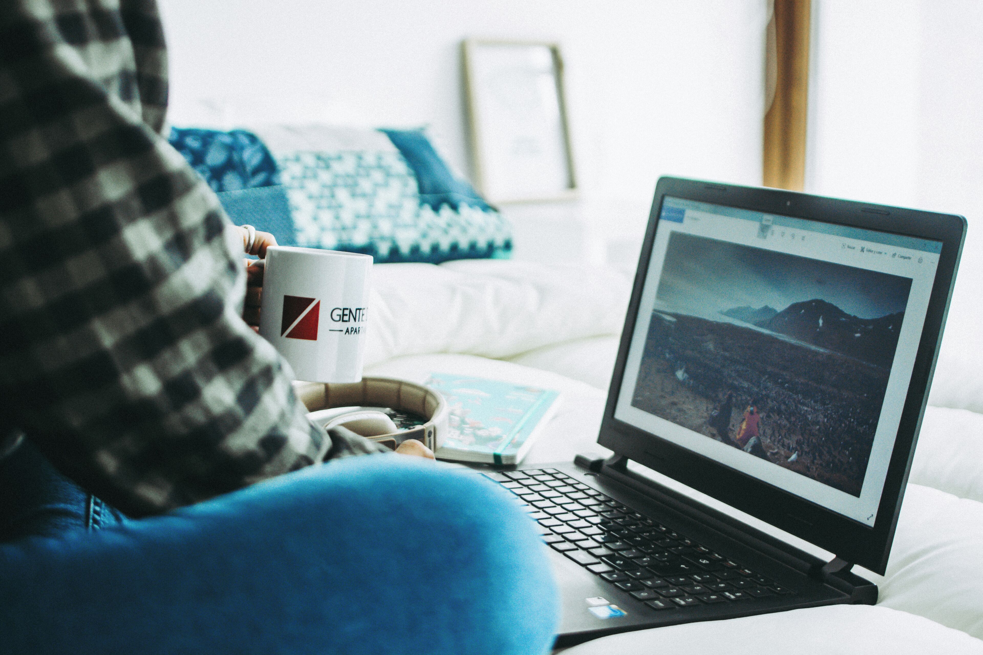 A laptop on a bed with a white pillow and a blue pillow in the background.