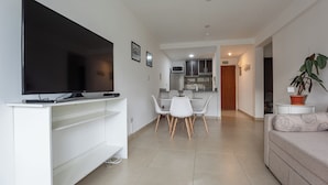 A modern living room with a flat-screen TV on a white entertainment unit, a dining area with a white table and chairs, and a kitchen in the background. - Gente del Sur - Amundsen (Ushuaia)