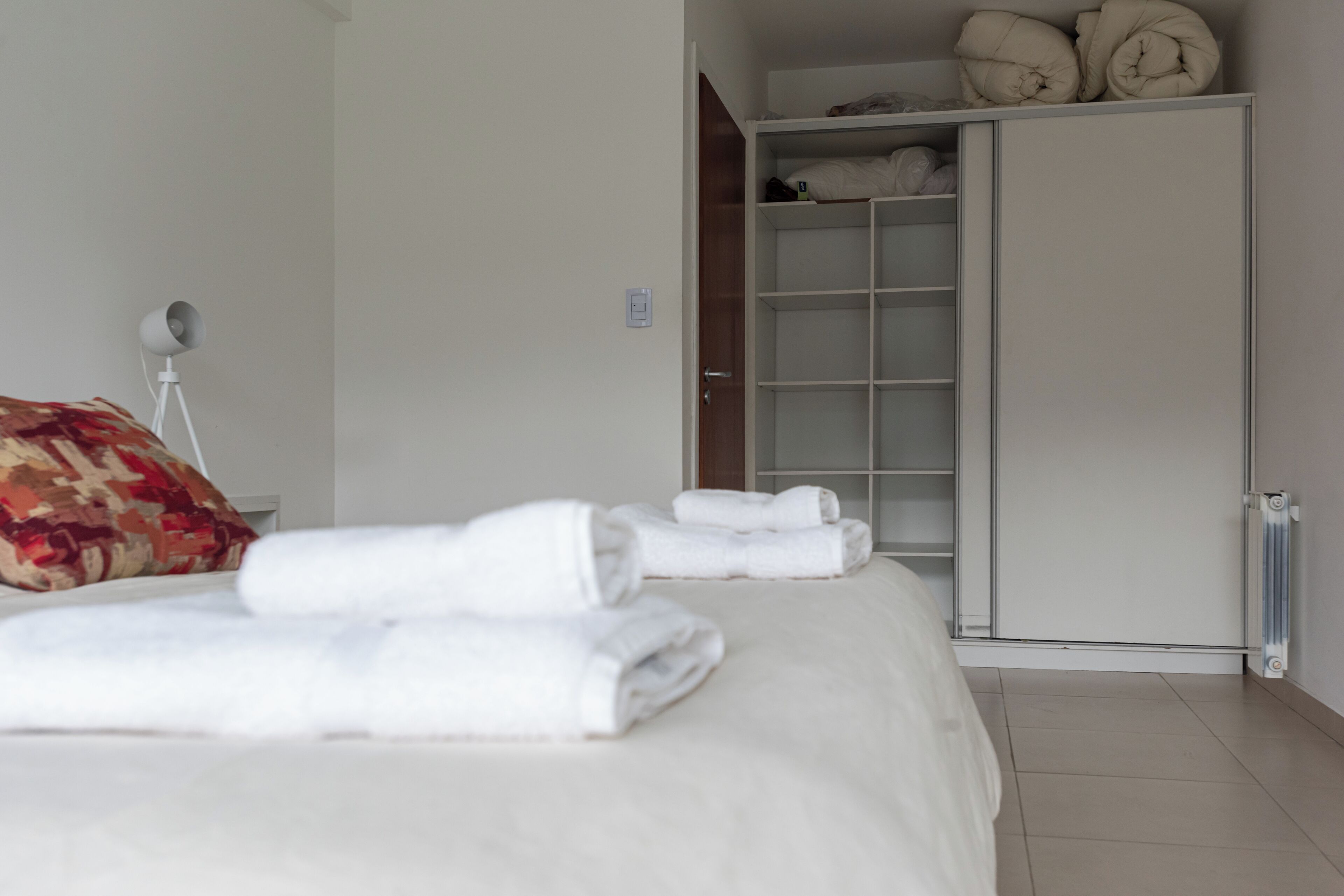 A neatly made bed with folded towels, a bedside lamp, and a wardrobe with shelves.