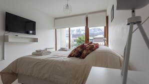A bedroom with a bed, a mounted TV, a bedside table, and a window with a mountain view. - Gente del Sur - Amundsen (Ushuaia)