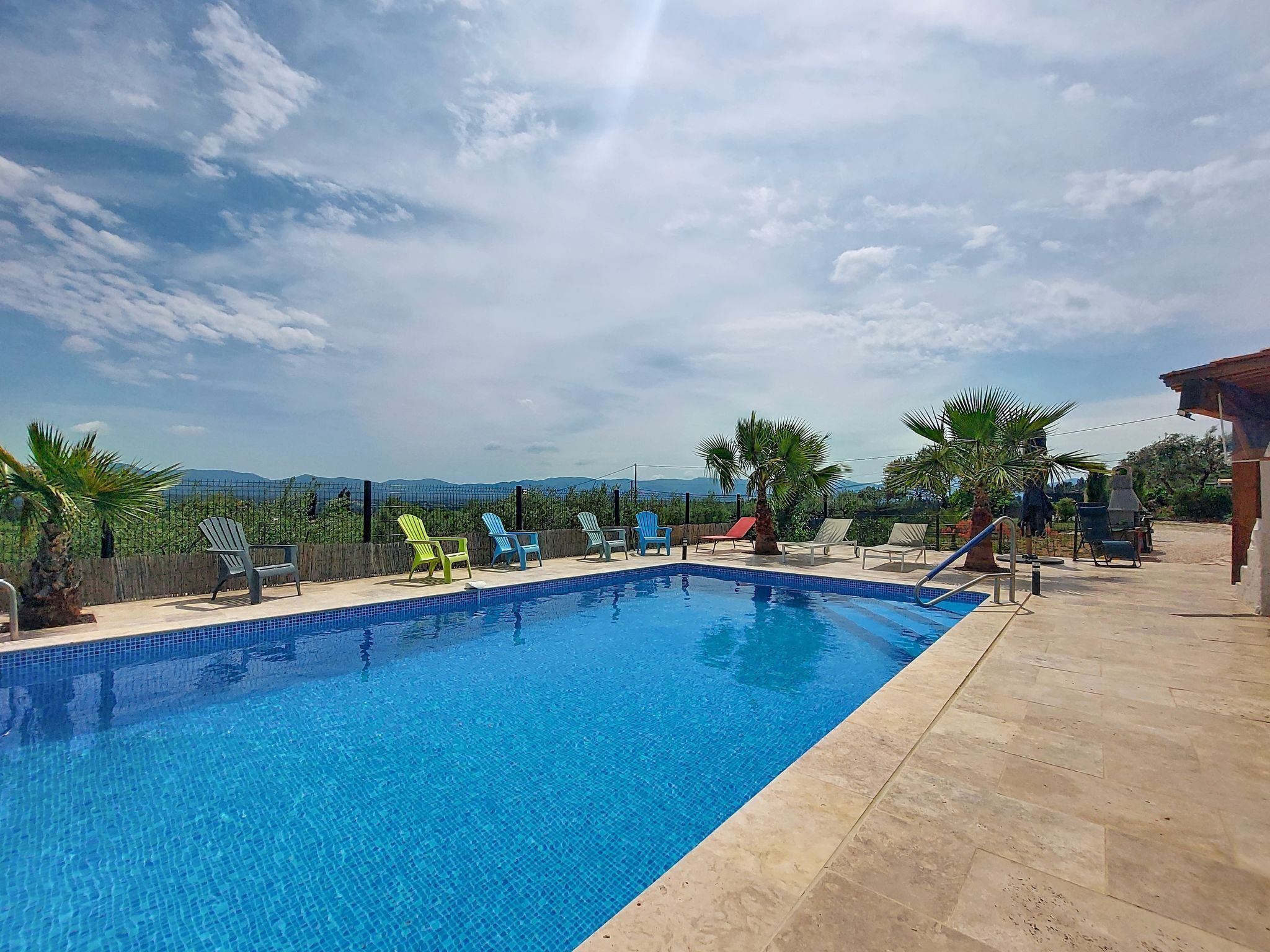 Une piscine avec des chaises longues, un palmier et une vue sur les montagnes lointaines.