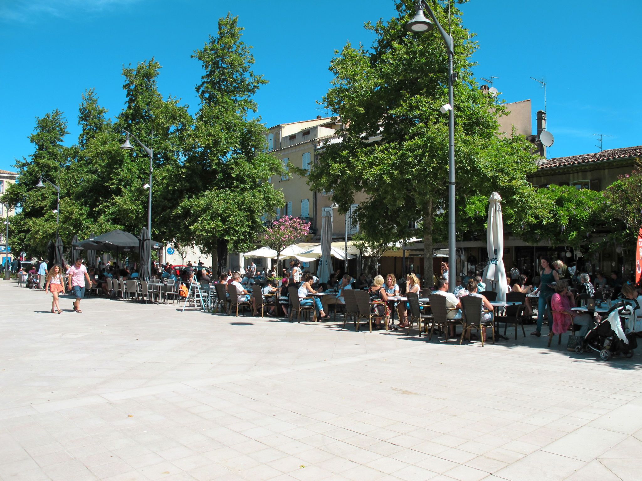 Un espace de café en plein air, avec des tables et des chaises, entouré d’arbres et de bâtiments.