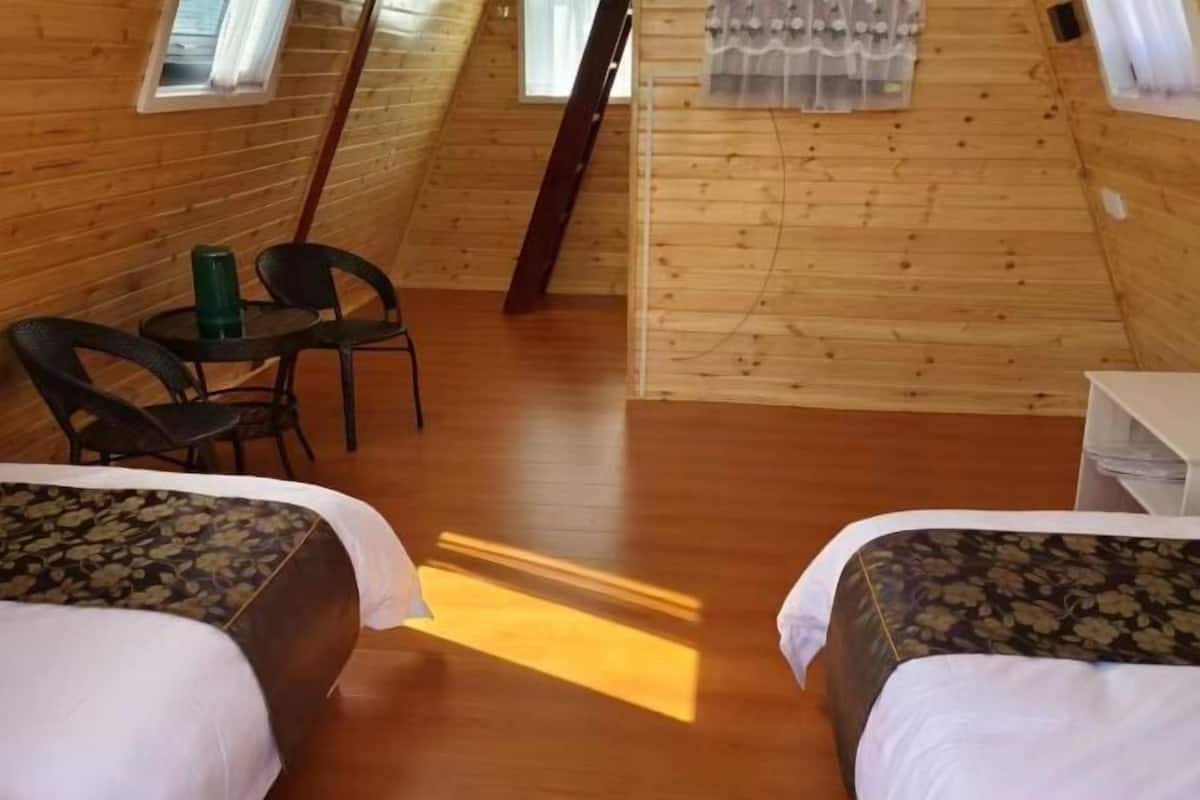 A wooden cabin with two beds, a small table, and chairs.