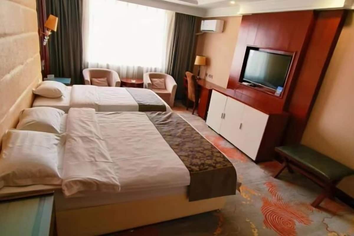 A hotel room with two beds, a TV, a desk, and a chair.
