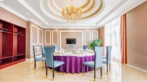 A dining area with a round table set for four, surrounded by blue chairs. A chandelier hangs from the ceiling, and a flat-screen TV is mounted on the wall. - Manzhouli Jinlongquan Hotel (Zhayanuoer Museum) (Hulunbuir)