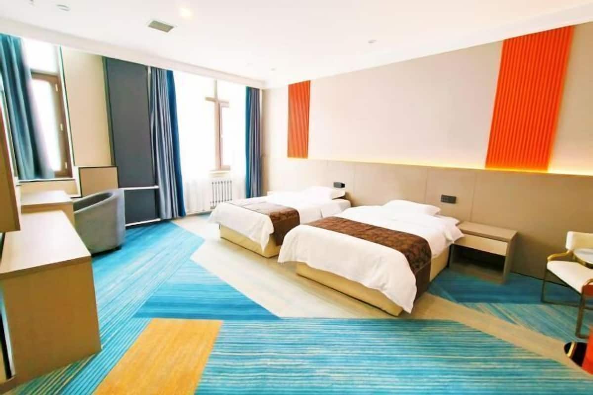 A hotel room with two beds, a desk, and a TV.