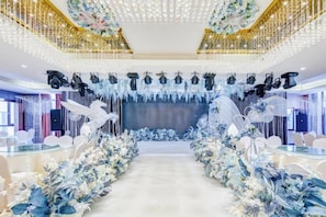 Un espace intérieur vaste et lumineux, avec une allée centrale, des compositions florales décoratives et un plafond orné de luminaires suspendus.