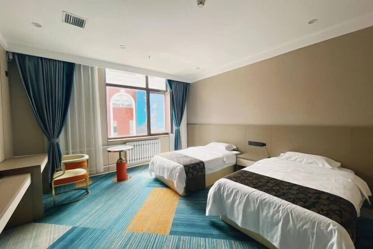 A hotel room with two beds, a desk, a chair, and a window with curtains.