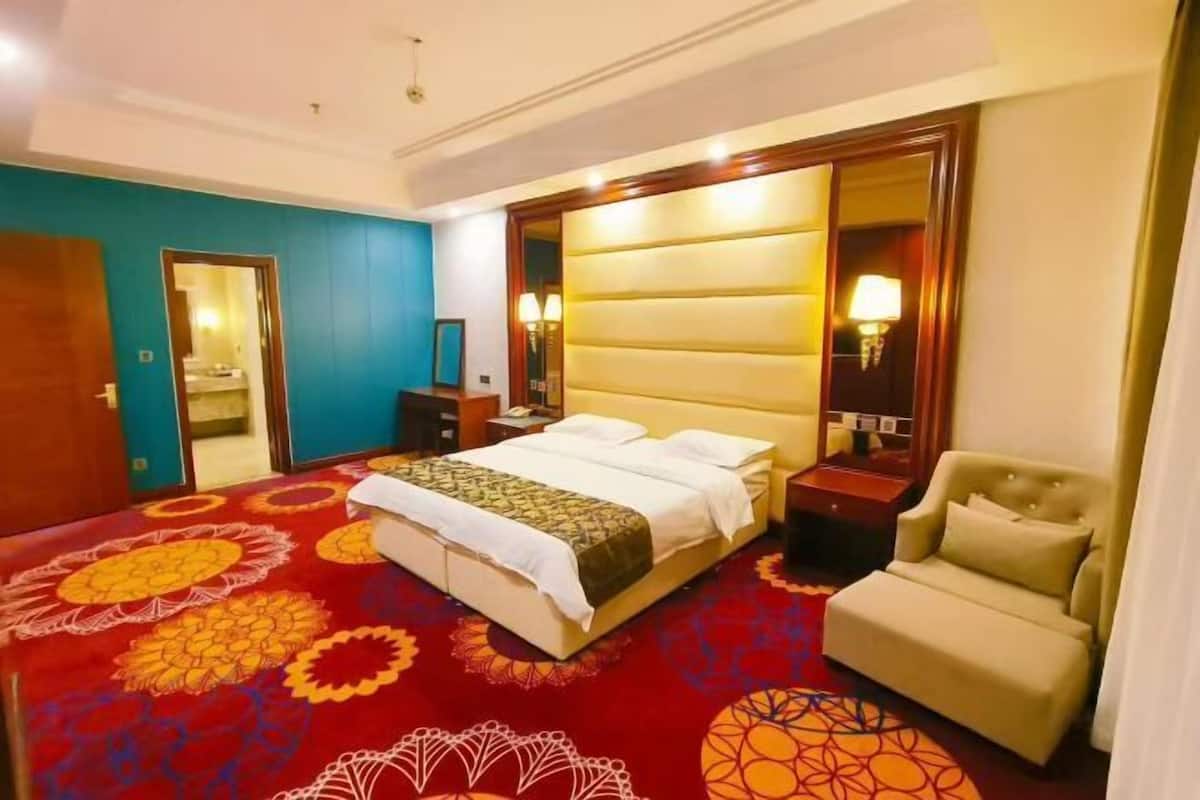 A hotel room with a large bed, a bedside table, a chair, and a mirror.