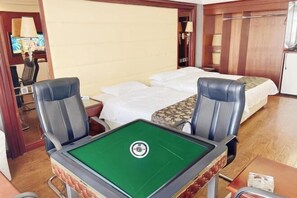 A hotel room with a green pool table, two single beds, a desk with a lamp, and a television.