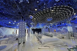 Une pièce dotée d’un luminaire circulaire au plafond, de chaises blanches et d’une scène.