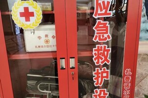 Entrada de sala de emergencias color rojo con puertas de vidrio, un bolso médico blanco y un emblema de la cruz roja.