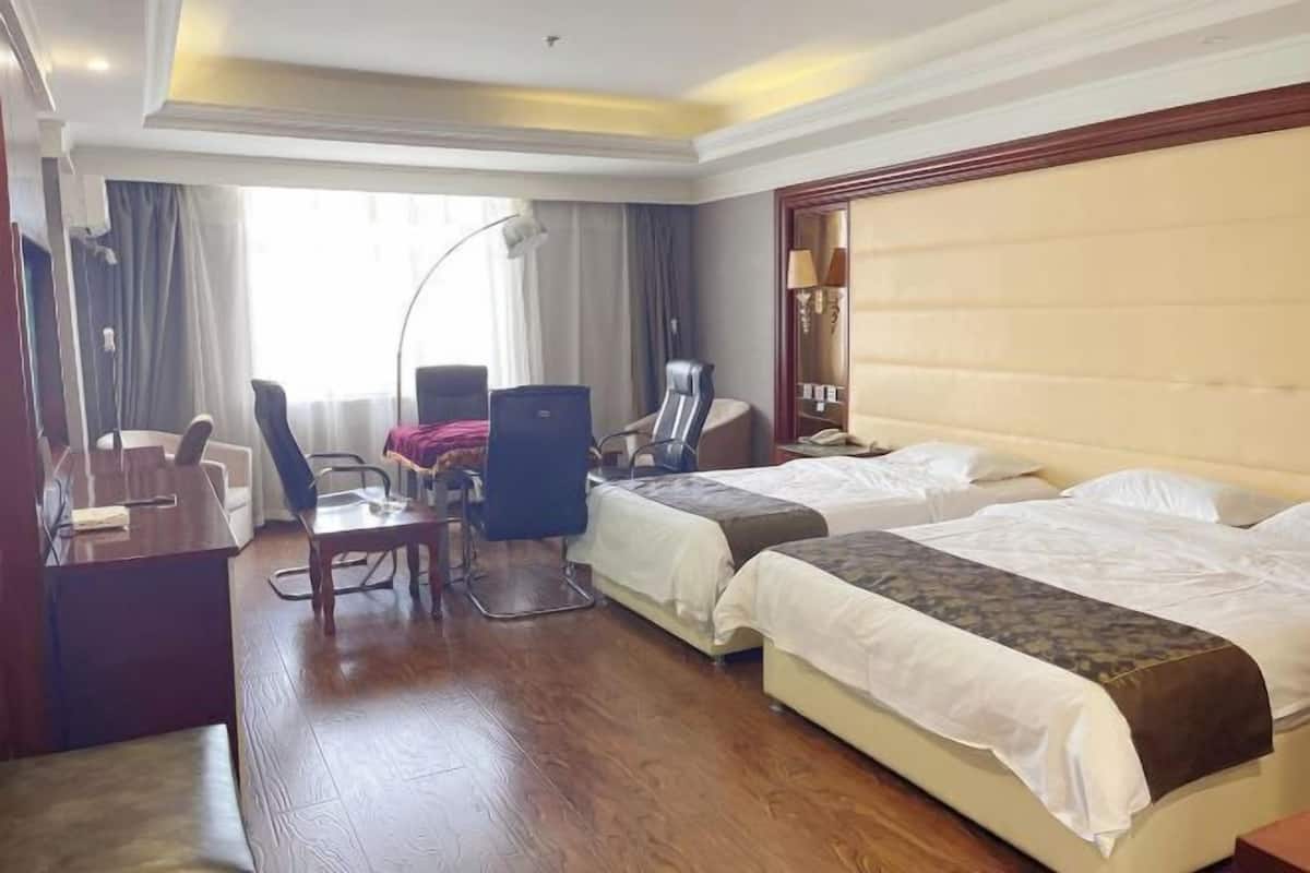 A hotel room with two beds, a desk, a chair, and a lamp.