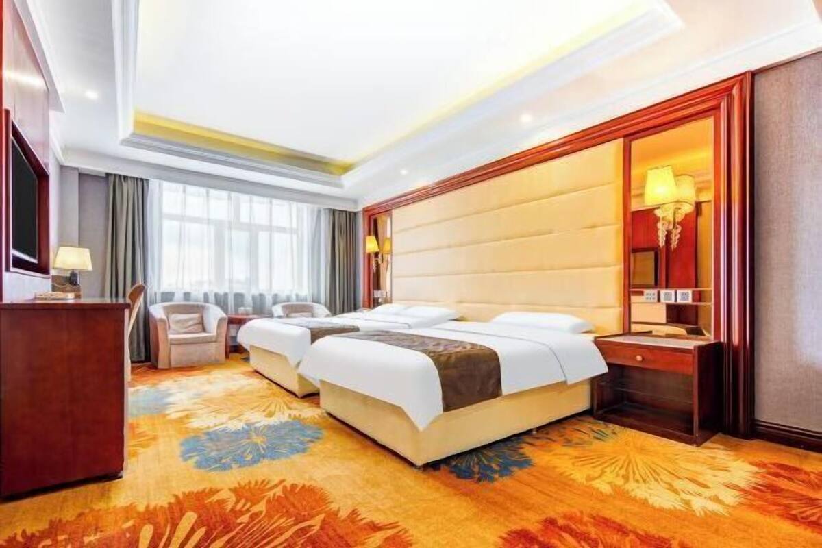 A hotel room with a large bed, a desk, a chair, and a window with curtains.