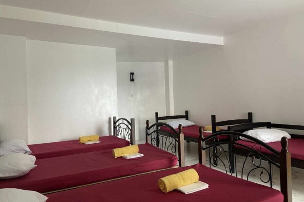 A room with four single beds, each with a red bedspread and white pillows.