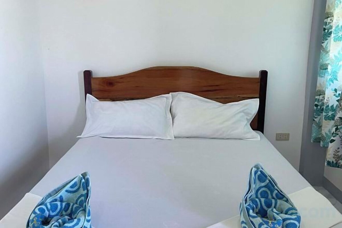 A bed with a wooden headboard, white bedding, and a blue patterned pillow on the left side.