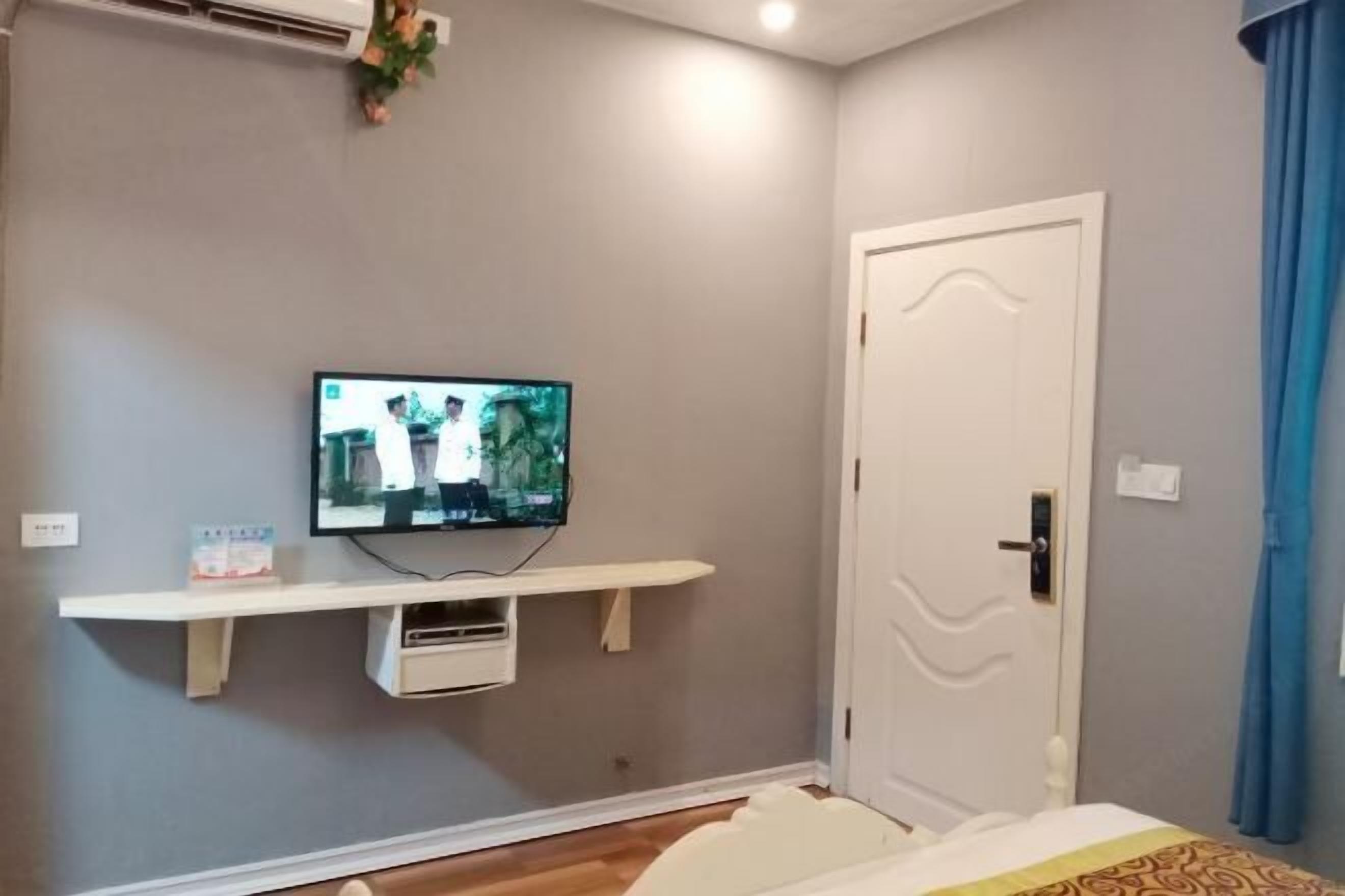 A bedroom with a bed, a TV mounted on a wall, a door, and a window with curtains.
