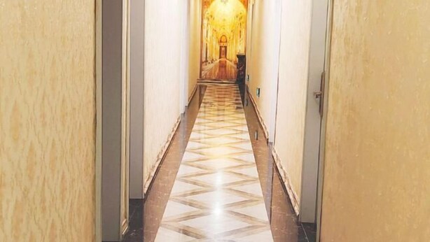 Corredor com piso estampado que leva a um quarto bem iluminado com um lustre.